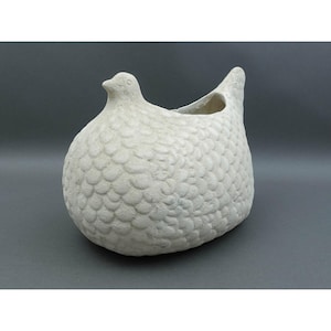 May include: A white, bird-shaped ceramic planter with a textured, scale-like pattern. The planter has a rounded body, a small head, and an opening at the top for plants or flowers. The neutral color and unique design make it a decorative item.