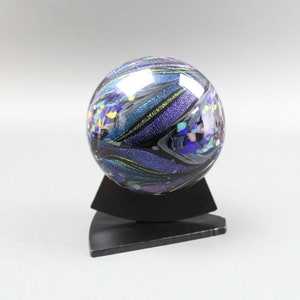 May include: A glass sphere with a black background and iridescent blue, purple, and green swirls. The sphere is on a black stand.