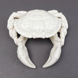 May include: A white ceramic crab figurine with detailed claws and a textured shell.