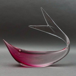 May include: A clear glass sculpture shaped like a fish with a pink, translucent body. The sculpture is designed to hold liquids.