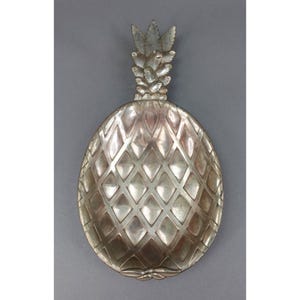 May include: Silver-colored pineapple-shaped decorative tray. The tray features a detailed design with a textured surface and a stem with leaves. The tray is designed to resemble a pineapple fruit.