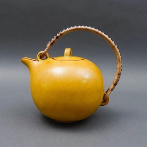 May include: A yellow ceramic teapot with a woven bamboo handle. The teapot has a rounded body and a lid.