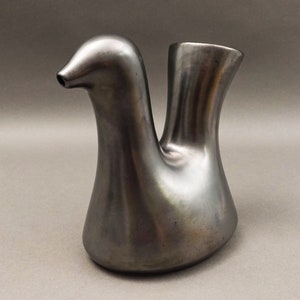 May include: A silver ceramic bird-shaped vase with a spout. The vase has a smooth, rounded surface and a sleek, modern design.