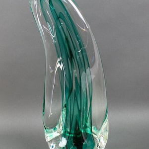 Könnte beinhalten: Eine klare Glasvase mit einer einzigartigen, organischen Form. Die Vase verfügt über wirbelnde, grüne Glasakzente, die einen dynamischen und modernen Look erzeugen.