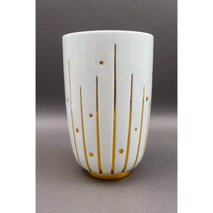 May include: White ceramic vase with gold vertical stripes and starburst accents. The vase has a gold base and a cylindrical shape. This decorative vase is suitable for displaying flowers or as a standalone art piece.
