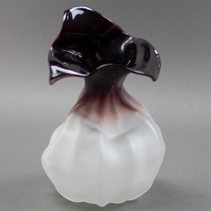 Puede incluir: Un pequeño jarrón de vidrio blanco esmerilado con una parte superior plegada de vidrio oscuro y brillante.