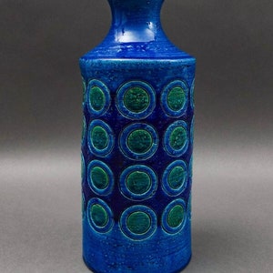May include: A blue ceramic vase with a geometric pattern of green circles. The vase has a narrow neck and a wide base.