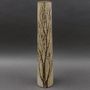 Puede incluir: Un jarrón cilíndrico de cerámica alto con un esmalte blanco y un diseño de árbol marrón. El jarrón mide aproximadamente 25 cm de alto.