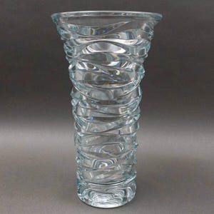 May include: A clear glass vase with a wavy, textured design. The vase is tall and slender, with a wide opening at the top and a narrow base.