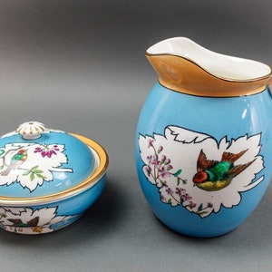 May include: A blue and white porcelain creamer and sugar bowl set with a bird and floral design. The creamer has a handle and the sugar bowl has a lid.