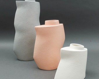 May include: Three ceramic vases of different sizes and colors. The largest vase is gray, the middle vase is peach, and the smallest vase is white.