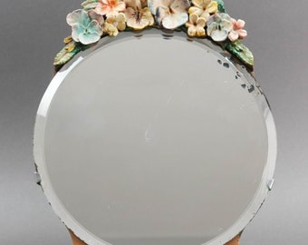 May include: A round, framed mirror with a decorative floral design. The mirror has a silver frame and is decorated with colorful flowers, including pink, blue, and yellow.