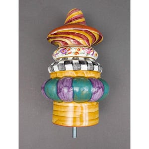 May include: A decorative ceramic finial featuring a stacked design with a spiraled red and yellow top, a floral band, a black and white checkered section, and a bulbous base with alternating teal and purple segments, ending in a metal bolt.