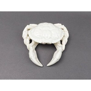 May include: A white ceramic crab figurine with detailed claw and shell textures. The crab is centered on a gray background, showcasing its intricate design. This decorative piece adds a coastal or nautical theme to home decor.