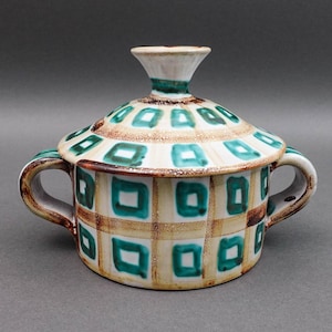 Könnte beinhalten: Eine Keramik-Zuckerdose mit Deckel, mit cremefarbenem Grund und einem Gittermuster aus braunen Linien und türkisfarbenen Quadraten. Der Deckel hat ein ähnliches Design. Die Schüssel hat zwei Griffe und einen weißen Knauf. Ein dekorativer Küchenartikel.