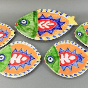 May include: Set of five ceramic fish-shaped plates with colorful designs. The plates feature green, blue, red, orange, and yellow colors. The plates are perfect for serving appetizers or snacks.