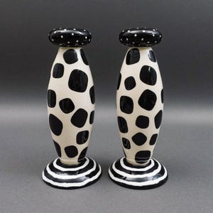 May include: Pair of decorative ceramic candle holders. The candle holders are off-white with large black polka dots. The base is black and white striped, and the top is black with white polka dots. The candle holders are approximately 25 cm tall.