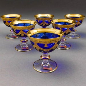 May include: Set of six cobalt blue and gold-rimmed stemmed glasses. The glasses have a decorative gold design around the rim and base.