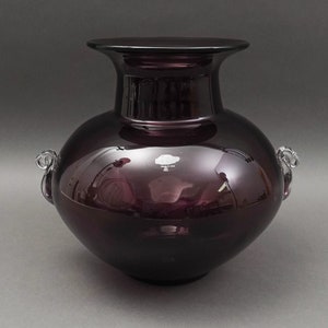 Può includere: Un grande vaso di vetro di colore viola scuro con due manici in vetro trasparente. Il vaso ha un corpo arrotondato e un bordo largo e piatto. Il vaso è fatto negli Stati Uniti.