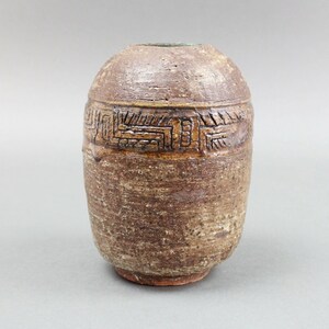 May include: A small, brown ceramic vase with a geometric design around the middle. The vase has a rough, textured surface.