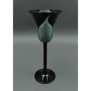 Può includere: Un vaso alto ed elegante in vetro nero con la parte superiore svasata e un lungo stelo. Il vaso presenta un design a piume stilizzato, azzurro e bianco sul davanti. La base è rotonda e nera. Il vaso è probabilmente per scopi decorativi.