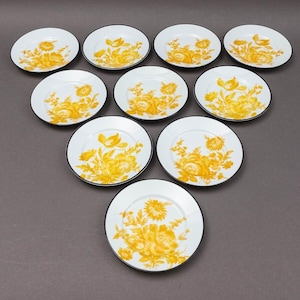Puede incluir: Diez platillos de cerámica blanca con borde negro y diseño floral amarillo.