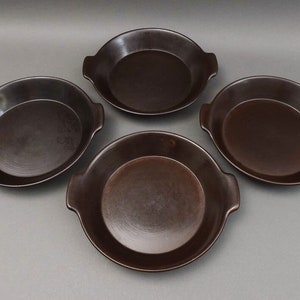 Puede incluir: Cuatro platos para hornear de cerámica marrón con asas. Los platos son redondos y tienen un borde ligeramente elevado.