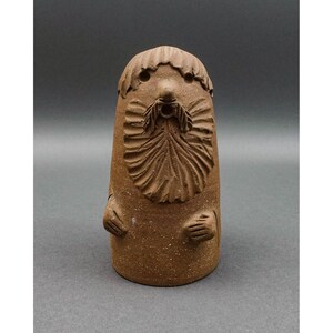 Puede incluir: Figura de cerámica marrón de un hombre barbudo con una larga barba y las manos juntas. La figura tiene una superficie texturizada y probablemente está hecha a mano. La figura tiene un estilo caprichoso y de arte popular.
