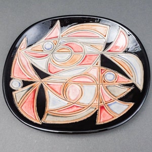 May include: A black ceramic plate featuring a stylised design of two fish in shades of pink, orange, blue and white.