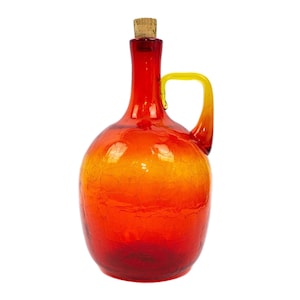 Puede incluir: Una botella de vidrio roja y amarilla con un tapón de corcho y un asa. La botella tiene una superficie texturizada.