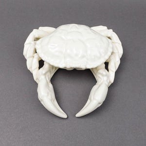 May include: A white ceramic crab figurine with detailed claws and a textured shell.