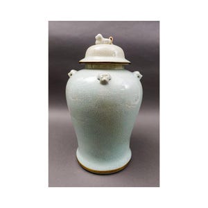 Peut inclure: Un vase en céramique de couleur céladon avec un couvercle. Le vase présente un glaçage craquelé et est orné de petites poignées en forme d'animal et d'un bouton sur le couvercle. La base et le bord sont garnis d'une bande dorée.