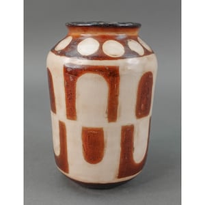 Puede incluir: Un jarrón de cerámica blanca con un patrón geométrico marrón. El jarrón tiene un cuerpo redondeado y un labio ligeramente acampanado.