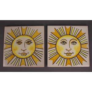 May include: Two ceramic tiles featuring a yellow sun face design. Each tile depicts a yellow sun with a smiling face, black eyes, and a yellow background. The sun has yellow and white rays.