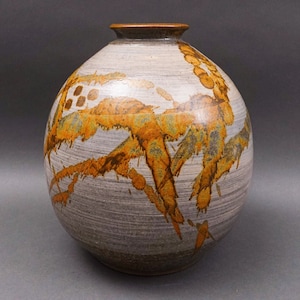 May include: A round ceramic vase with a white glaze and brown and orange abstract designs.