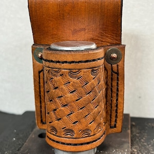 May include: A brown leather tool holder with a tooled design and a metal loop. The holder has a metal snap closure and is designed to hold a small tool or other object.