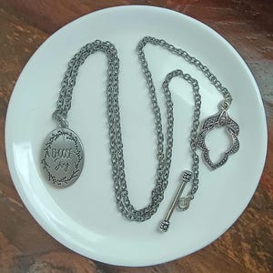 May include: Silver necklace with a round pendant that says "Choose Joy" surrounded by a wreath design. The necklace has a silver chain and a silver clasp.