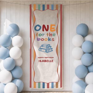 May include: A vertical rectangular banner featuring a cream-colored center with a wavy border and colorful vertical stripes on the sides. The text reads ONE for the books, HAPPY BIRTHDAY ISABELLE, with a blue line drawing of three stacked books.