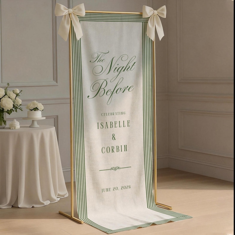 May include: A tall, rectangular fabric banner with green striped borders, suspended from a gold metal frame with cream-colored bows. The banner features the text: The Night Before, CELEBRATING ISABELLE & CORBIN, JUNE 20, 2026, in green lettering.