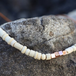 May include: A simple necklace with white wooden beads and a row of rose gold square beads.