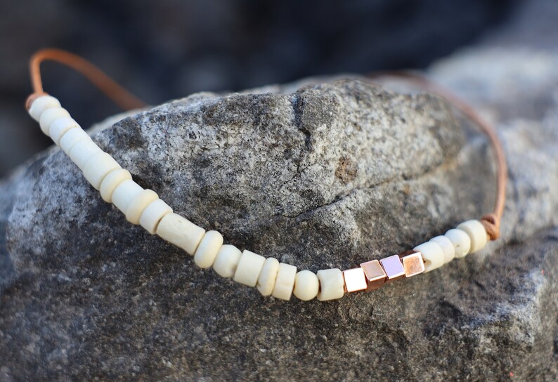 May include: A simple necklace with white wooden beads and a row of rose gold square beads.