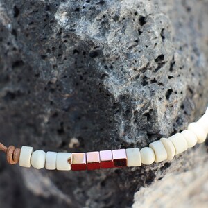 May include: A brown leather cord necklace with white and rose gold square beads.