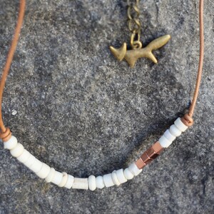 May include: A brown leather cord necklace with white beads and a copper accent. A small gold fox charm hangs from the cord.