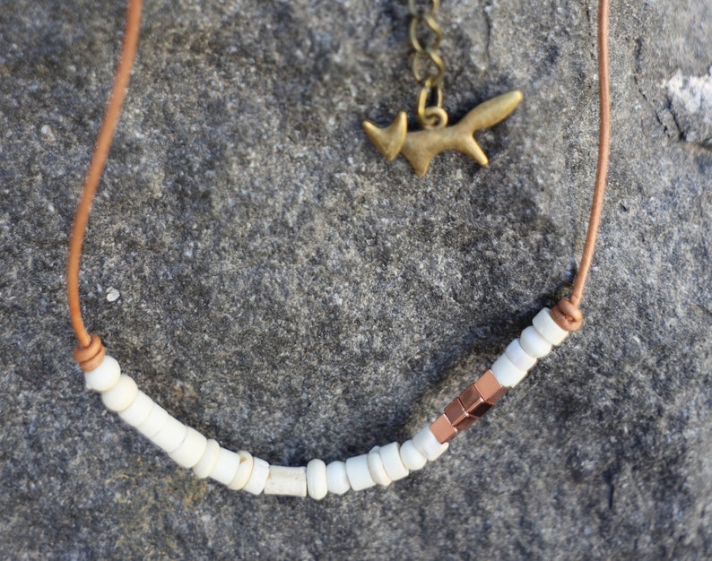 May include: A brown leather cord necklace with white beads and a copper accent. A small gold fox charm hangs from the cord.