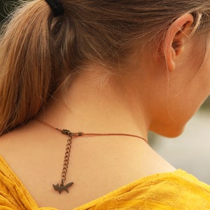 May include: A woman with long blonde hair pulled back in a ponytail is wearing a yellow shirt and a brown leather cord necklace with a small fox charm.