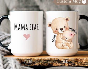May include: White ceramic mug with a black rim and handle. The front of the mug says "Mama Bear" with a pink heart. The back of the mug has a cartoon illustration of a brown bear mom holding a smaller brown bear cub. The text "Mom" is above the bears and "Sophia" is to the right of the bears.
