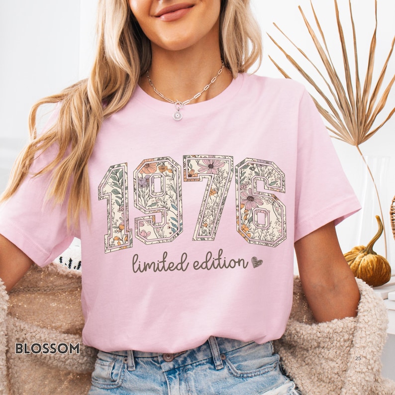 Peut inclure: T-shirt rose clair avec l'ann&eacute;e "1976" dans un motif floral. Les mots "limited edition" sont imprim&eacute;s en dessous. Le t-shirt a un col rond et des manches courtes.