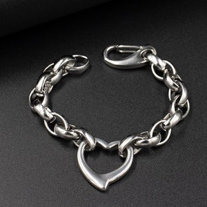 May include: A silver chain bracelet with a heart-shaped charm. The bracelet is made of a thick, chunky chain.