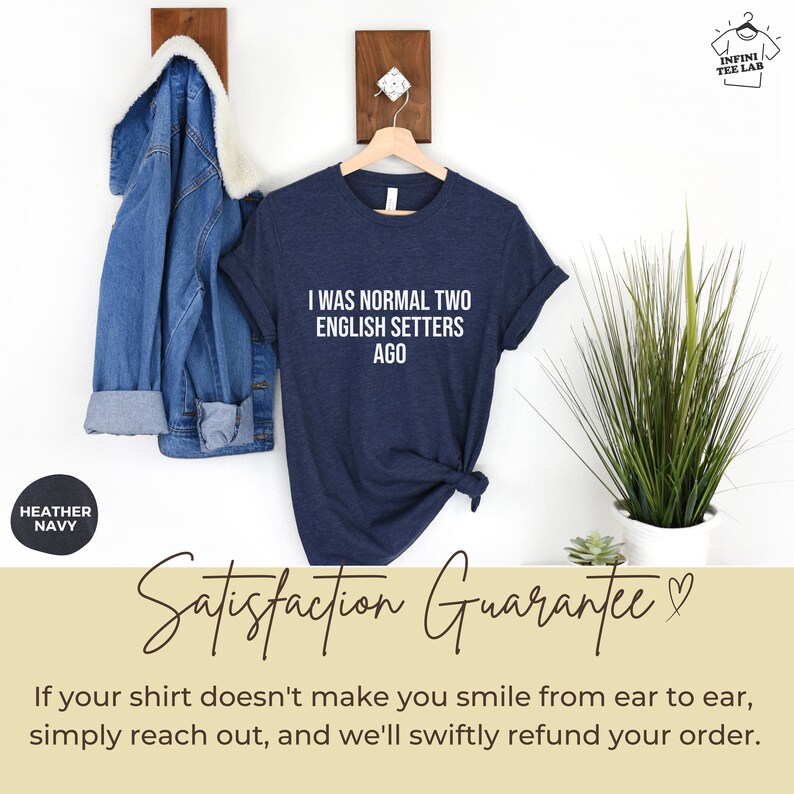 May include: A heather navy blue t-shirt with the text "I was normal two English Setters ago" printed in white. The shirt is hanging on a hanger against a white wall. The text "Satisfaction Guarantee" is written in cursive on a beige background.