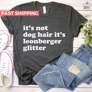 Könnte beinhalten: Ein dunkelgraues T-Shirt mit dem Text "it's not dog hair it's leonberger glitter" in weißen Buchstaben.